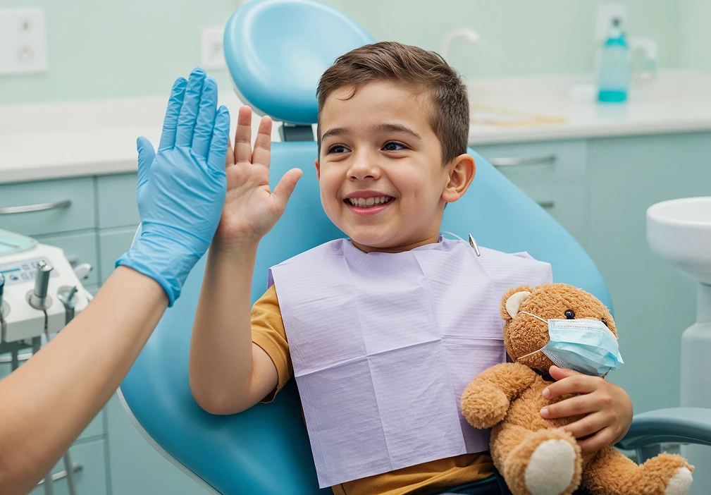 Cheerful boy is giving a high five to a dental professional while holding a teddy bear in a dental clinic.